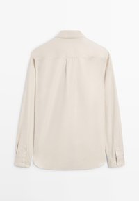 Chemise beige à manches longues avec poignets boutonnés, empiècement dos et un pli central, vue de dos sur fond blanc.