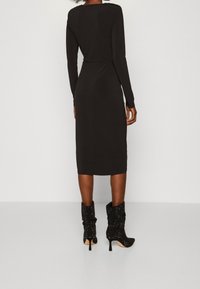 Czarna, długosleeve sukienka z dopasowaną talią i długości midi, zestawiona z luźnymi czarnymi szpilkami o błyszczącej teksturze.