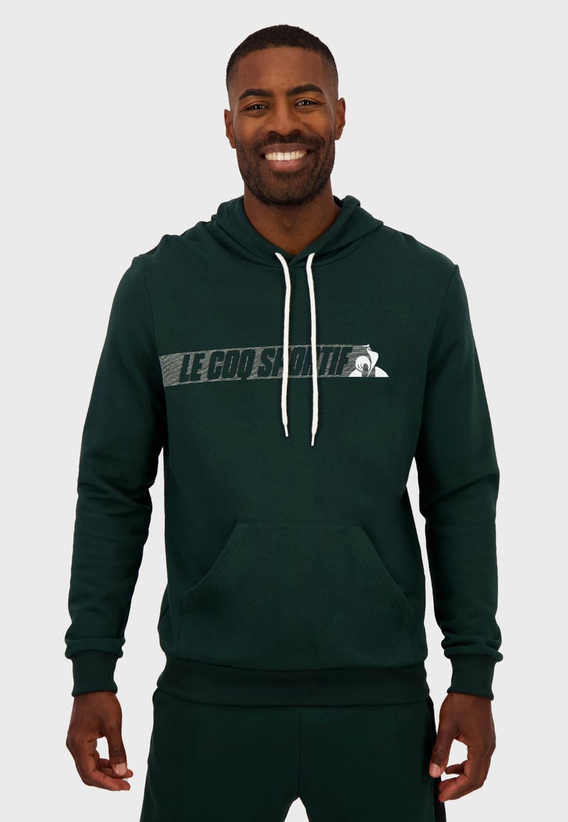 Sudadera verde oscura hecha de material suave, con un bolsillo canguro, capucha con cordón y un logo impreso en blanco en el pecho.