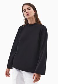 Czarna bluza z długim rękawem i wysokim kołnierzem, wykonana z miękkiego materiału. Design z opadającymi ramionami i luźnym fasonem.