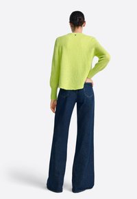 Neon groene wollen trui met een losse pasvorm, ronde hals en geribbelde manchetten, gecombineerd met donkerblauwe jeans met wijde pijpen.