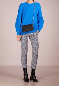 Pull tricot bleu vif, pantalon à carreaux noir et blanc, bottines noires brillantes et sac bandoulière noir avec des accents métalliques.
