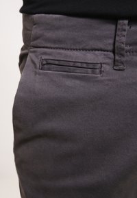 Szare spodnie z tkaniny o gładkiej fakturze, z płaską przednią kieszenią oraz czystym wzorem paska w pasie. Kolor jest jednolity, bez widocznych wzorów.