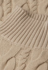 Beige gestrickter Stoff mit Rippenmuster, der in ein Zopfmuster übergeht, zeigt Textur und Maschen-Details.