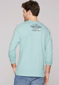Licht turquoise lange mouwen shirt met een ronde hals, voorzien van zwarte grafische tekst op de rug en een ontspannen pasvorm. Zachte textuur, casual stijl.