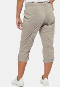 Pantalons cropped beige avec une coupe décontractée, dotés de deux poches arrière, d'une taille élastique et de poignets roulés. Portés avec des baskets blanches.