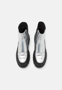 Botas de tobillo metálicas plateadas con un diseño elegante, suela de goma negra y paneles texturizados en la zona de los dedos. Sin detalles de hardware visibles.