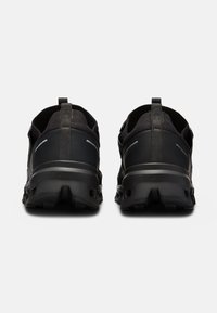 Chaussures de sport noires avec une semelle en caoutchouc durable, une tige en maille et des accents réfléchissants. Elles présentent un design épuré et un col rembourré pour plus de confort.