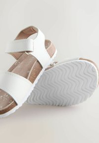Sandală albă cu două barete late, cataramă reglabilă, talpă mijlocie din plută și talpă exterioară albă texturată din cauciuc, cu model în valuri.