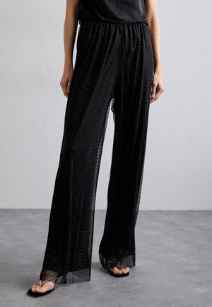 Zwarte transparante broek met een losse pasvorm, voorzien van een textuurpatroon en een elastische tailleband. Accenten zijn onder andere een golvende zoom en zijsplitten.
