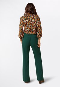 Multicolored floral blouse with puffed sleeves paired with high-waisted green trousers, featuring a smooth texture and tailored fit.