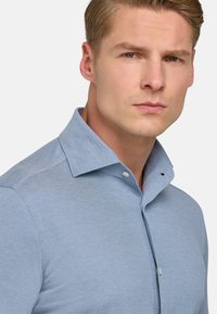 Camicia azzurro chiaro con tessuto testurizzato. Presenta un colletto medio e bottoni bianchi, con un design aderente.