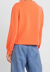 Helle orange Sweatshirt mit langen Ärmeln, gerippten Bündchen und lockerer Passform, kombiniert mit hellblauen, leicht lockeren Denim-Hosen.