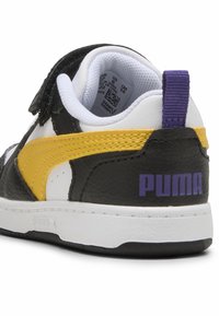 Fekete-fehér sneaker sárga és lila kiegészítőkkel, struktúrált felsőrésszel, tépőzárral és márkázott sarokpánttal.