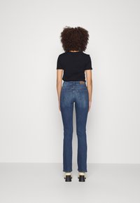 Vaqueros de mezclilla azul de tiro alto con corte recto, que cuentan con dos bolsillos traseros y una etiqueta de marca de cuero marrón. Camiseta negra de manga corta.