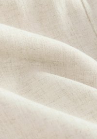 Luonnollinen pellavakangas, vaalean beige väri, pehmeä rakenne, jossa on hienovarainen kudos sekä lieviä poimuja ja vaihtelevaa langankulkua.