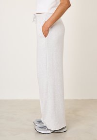 Gaiši pelēkas sporta bikses no mīksta auduma ar brīvu piegriezumu, sānu kabatām un elastīgu jostasvietu ar aukliņu.