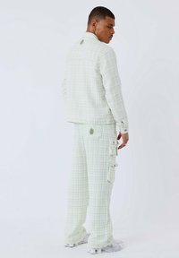 Lichtgroene geruite jas en bijpassende broek van textuurstof. Bevat cargo pockets en een subtiele merkvermelding op de achterkant.