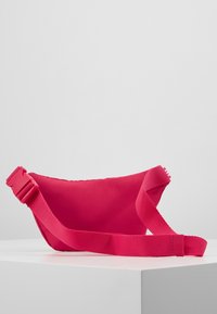 Rosa tyg crossbody-väska med en texturerad yta, justerbar rem och spännclosure. Kompakt form med rundade kanter.