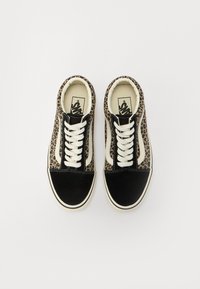 Une paire de baskets Vans imprimées léopard et noires avec des lacets blancs, vues du dessus sur un fond blanc.