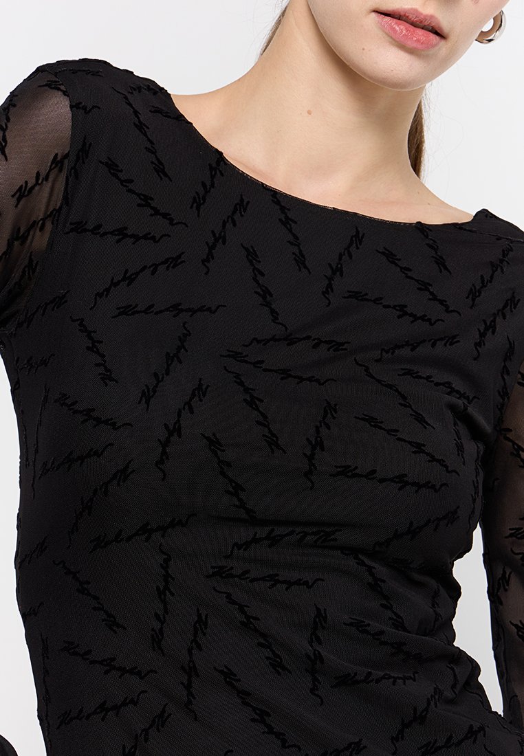 Top negro con mangas largas de tul transparente, que presenta un patrón texturizado de líneas en zigzag y un escote barco. Tejido suave con una silueta ajustada.