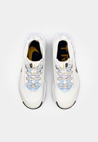 Baskets de sport blanches avec une tige en mesh, des accents bleus et jaunes, et des lacets argentés réfléchissants. Semelle arrondie avec une semelle extérieure en caoutchouc noir.