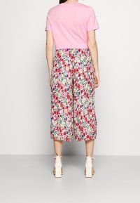 T-shirt rose court associé à un pantalon culotte à imprimé floral avec des fleurs roses, rouges et vertes sur un fond jaune clair. Sandales à talons blocs.