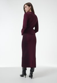 Vestido burdeos de manga larga con patrón de rayas negras texturizadas, silueta ajustada, abertura en la parte trasera, combinado con botas negras hasta la rodilla.