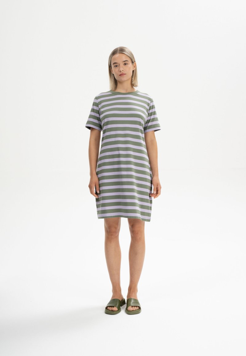 Gestreiftes Kurzarmkleid in Grün- und Lilatönen, aus weichem Stoff gefertigt. Das Kleid hat eine lässige Passform und endet oberhalb des Knies. Getragen mit grünen Rutschsandalen.