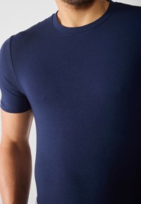 Marineblå kortermet t-skjorte laget av myk stoff, med rund hals og en tettsittende design med jevn tekstur.