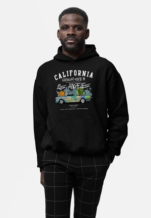 Homme portant un sweat à capuche noir avec un camion vintage style graffiti coloré et un texte faisant référence à la Californie et à Los Angeles.