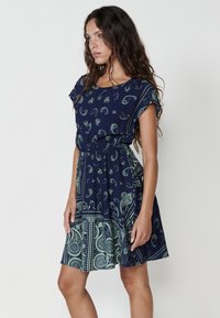 Rochie bleumarin cu model paisley verde, mâneci scurte, talie elastică și fustă evazată. Material moale cu o textură netedă.