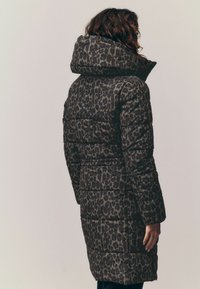 Dlhý, vyp padded kabát s leopardím potlačou v tmavých tónoch. Má veľkú kapucňu, elastické manžety a opasok v páse. Hladká textúra.