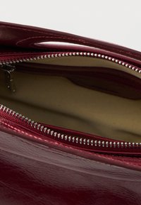 Δερμάτινη τσάντα μπορντό με ασημένιο φερμουάρ, με ανοιχτό πάνω μέρος και εσωτερικές θήκες, που παρουσιάζει ομαλή υφή και ανθεκτικό σχεδιασμό.