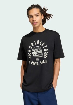 Młody mężczyzna z dredami, ubrany w czarny t-shirt w stylu wyścigowym z napisem „BORTOLETO”, hełmem i tekstem „São Paulo, Brazylia”.