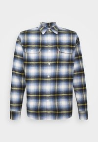Camicia di flanella caratterizzata da un motivo a quadri blu, bianco e giallo, con colletto classico e chiusura con bottoni. Include due tasche sul petto.