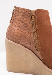 Botín de tacón cuña marrón con un diseño de serpiente texturizado en la parte trasera y una parte delantera de ante suave, con una cremallera lateral y una suela gruesa.