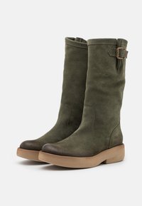 Bottes en suédine vert olive montant jusqu'au genou, avec un bout arrondi, arborant un accent marron sur le capuchon et un détail de boucle en métal sur la tige supérieure.