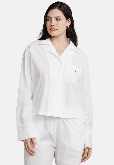 Camicia bianca a taglio corto in cotone con maniche lunghe, taschino sul petto e branding discreto sulla tasca. Tessuto liscio.