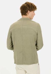 Olijfgroene jas met een gestructureerde afwerking, voorzien van een klassieke kraag en een rechte snit, met minimale details aan de achterzijde.