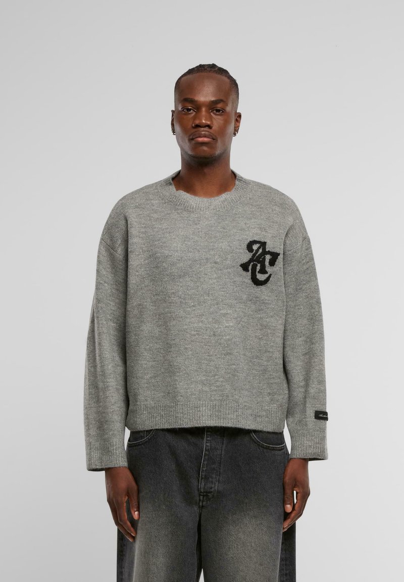 Maglione grigio lavorato a maglia con collo rotondo, vestibilità rilassata e dettaglio del logo nero sul petto. Tessuto testurizzato, polsini e orlo a costine.