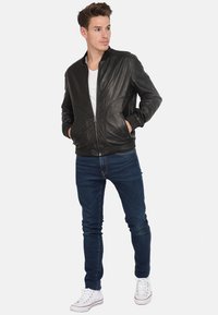 Zwarte leren bomberjack met ribgebreide manchetten, ritssluiting aan de voorkant en zijzakken, gecombineerd met donkerblauwe jeans en witte sneakers.
