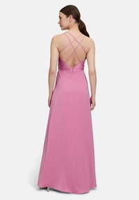 Długa różowa sukienka z dopasowanym gorsetem i skrzyżowanymi ramiączkami. Posiada głęboki dekolt w kształcie litery V z tyłu oraz gładki, zwiewny materiał.