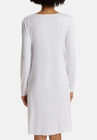 Abito bianco a maniche lunghe con scollatura rotonda, realizzato in un tessuto leggero, presenta una vestibilità ampia che arriva sopra il ginocchio.