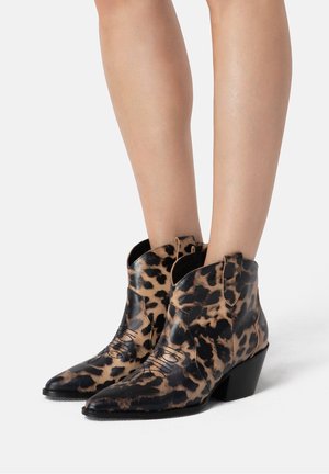 Bottes en cuir montant jusqu'à la cheville, bout pointu, motif léopard noir et marron, portées sur jambes nues.