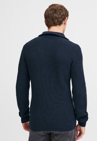 Navy knitted sweater, featuring a textured ribbed design, long sleeves, a shawl collar, and fitted cuffs, with a straight hemline at the back.