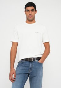 Balta kokvilnas T-krekls ar īsām piedurknēm, kreisajā pusē ar nelielu zilu tekstuālu logotipu. Kopā ar gaiši ziliem džinsa džinsiem un melnu jostu.