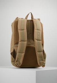 Brązowy plecak z materiału, z wyściełanym siatkowym tyłem, regulowanymi paskami i solidnym uchwytem na górze. Posiada zasuwaną główną przegrodę i minimalną ilość elementów metalowych.