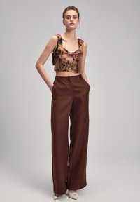 Brune bredbenede bukser med høj talje, parret med en blomstertrykt cropped top med sløjfedetalje og brede stropper, glat stoftekstur.