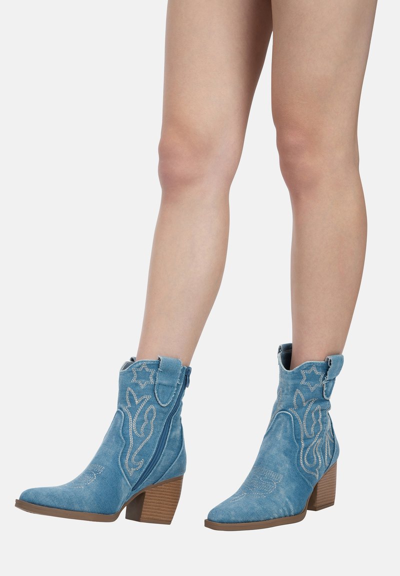 Botines de ante azul con punta afilada, costuras decorativas y tacón cuadrado. Presenta una cremallera y una lengüeta para facilitar su colocación.
